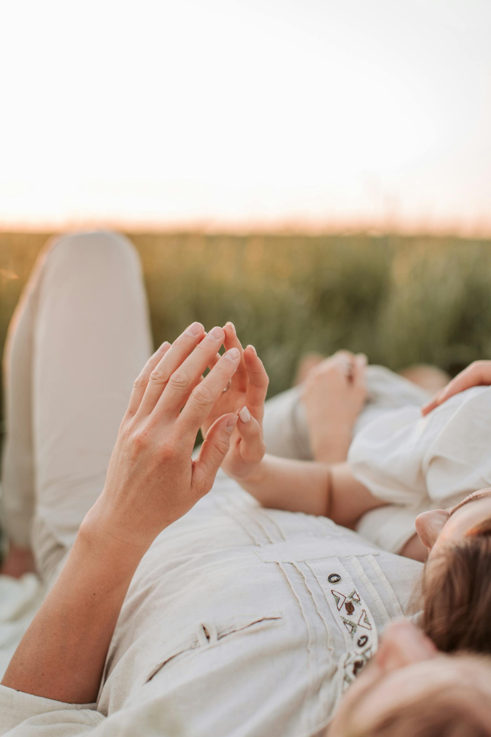A loving couple relaxes outdoors in a field at sunset, enjoying a romantic moment together.