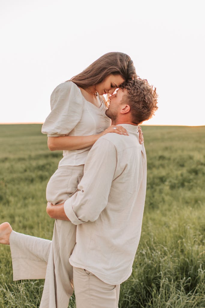 A loving couple shares a romantic embrace in a sunny grass field, symbolizing togetherness and joy.