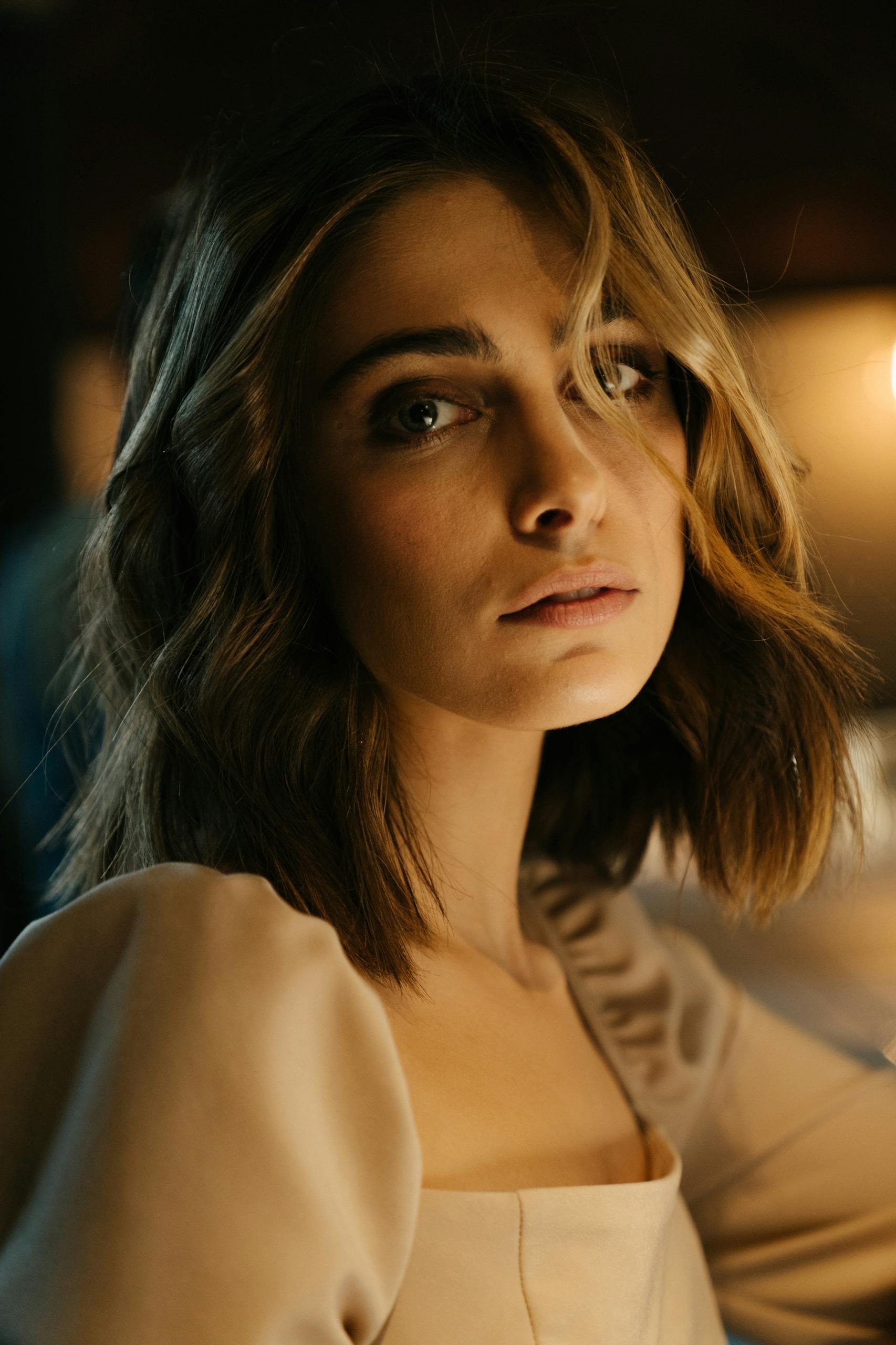 Portrait of an elegant woman sitting at a bar counter with a thoughtful expression in dim lighting.